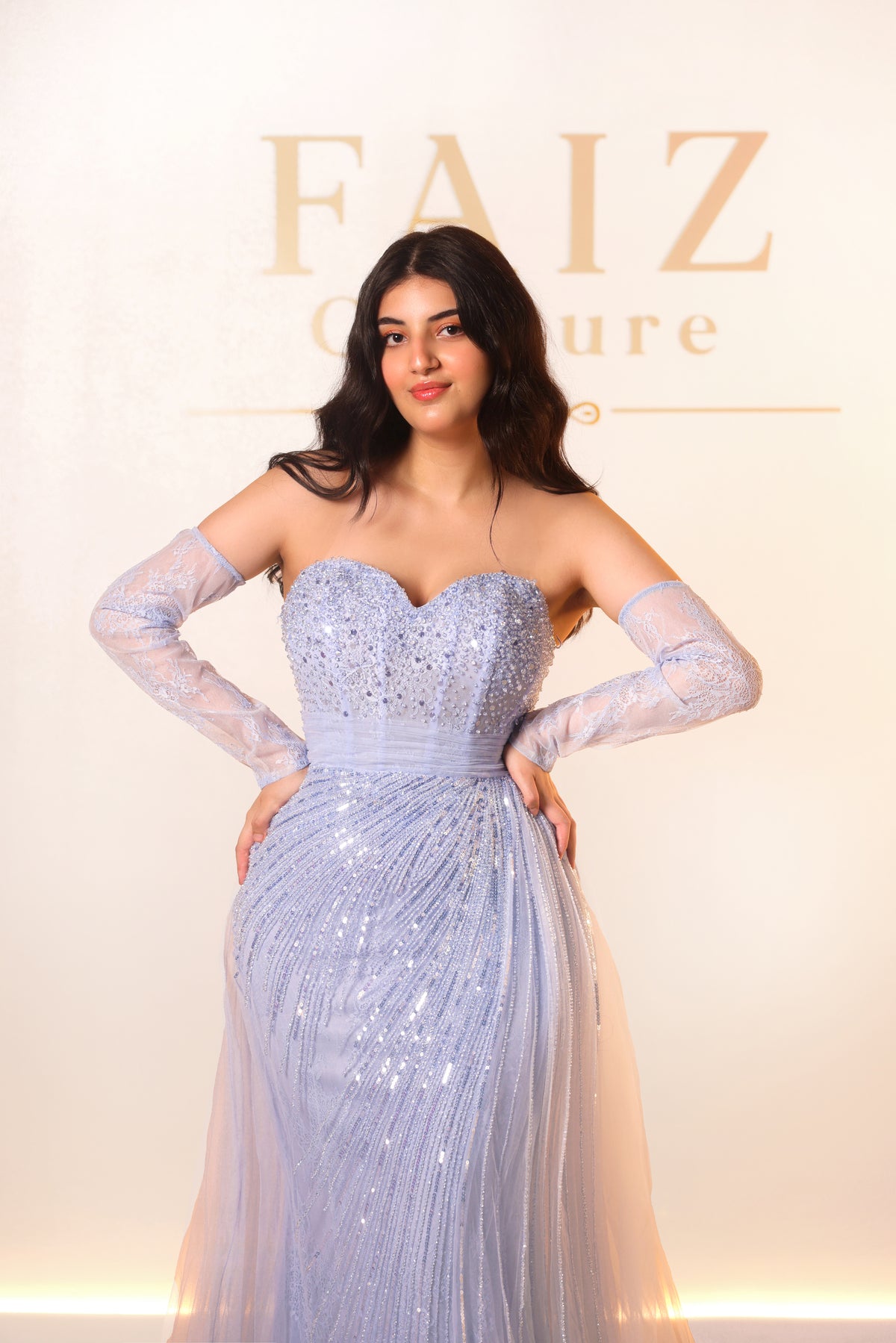 A woman modeling a light blue strapless gown with long sheer sleeves and a sweetheart neckline, FAIZ COUTURE