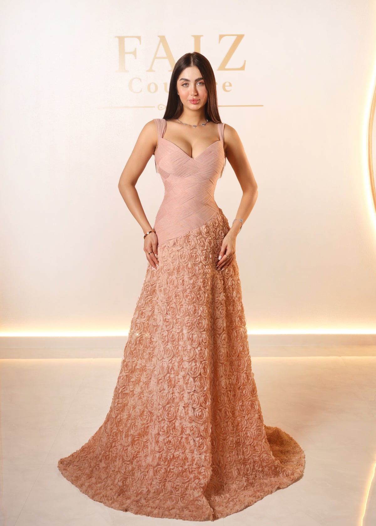 A woman modeling a floor-length evening gown in a warm blush pink color,  FAIZ COUTURE