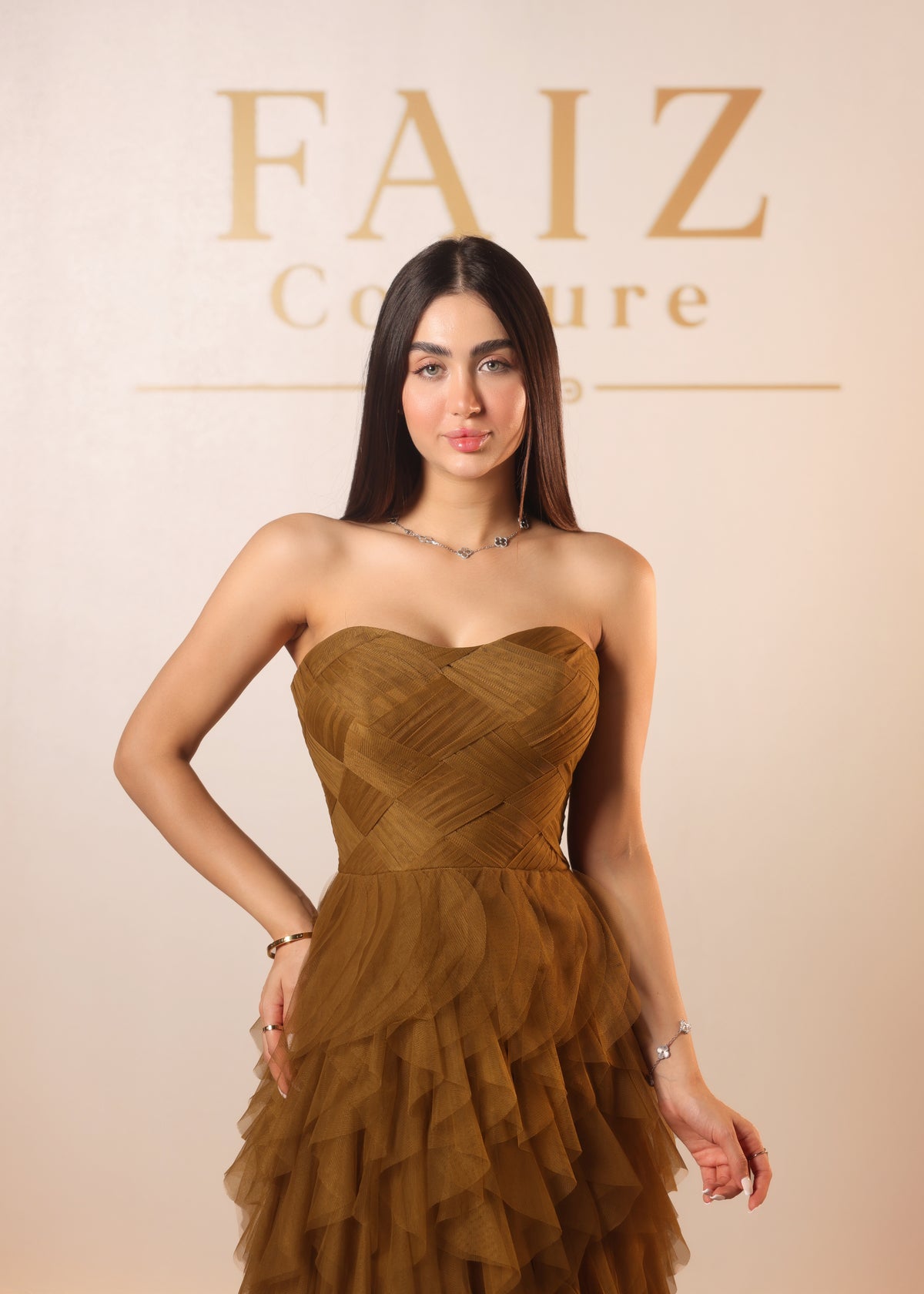A woman modeling a strapless brown dress with a structured sweetheart bodice and layered ruffled skirt, FAIZ Couture