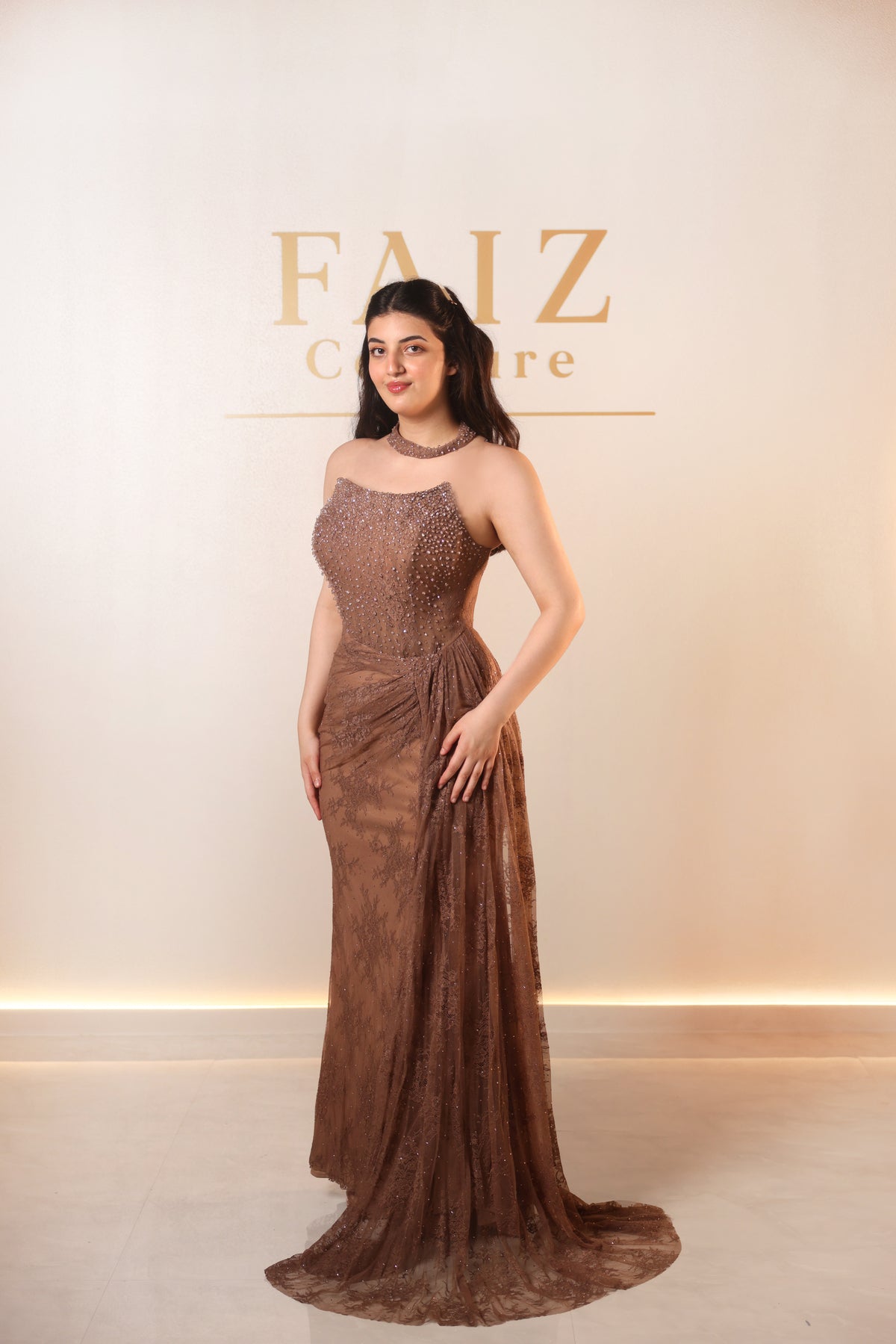 A woman modeling a floor-length brown lace gown with a sheer draped train, FAIZ COUTURE