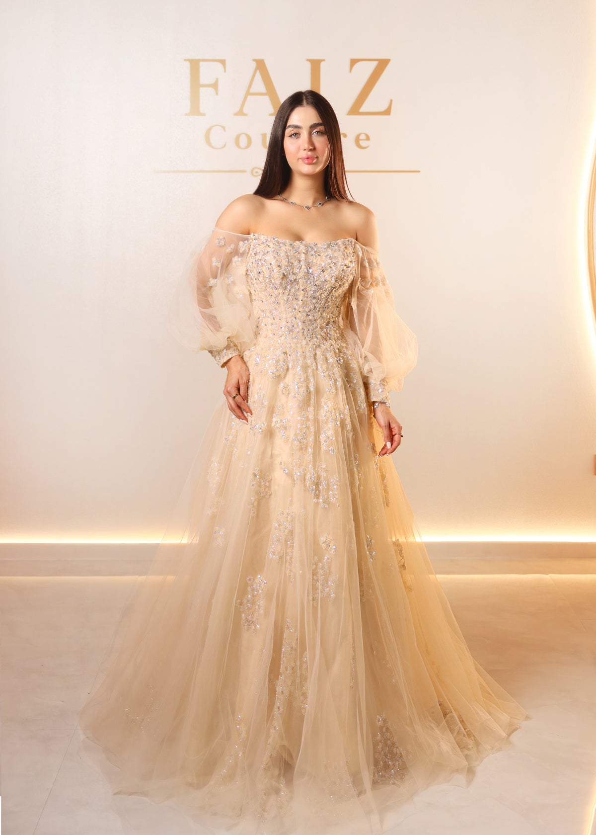 A woman modeling an off-the-shoulder champagne beige tulle gown with intricate floral embroidery and a full skirt, FAIZ COUTURE