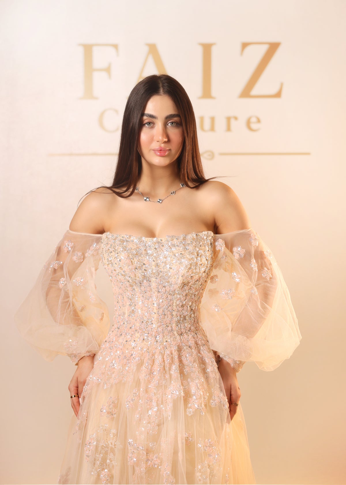 A woman wearing a champagne off-the-shoulder gown with intricate beadwork and voluminous sheer puff sleeves, FAIZ COUTURE