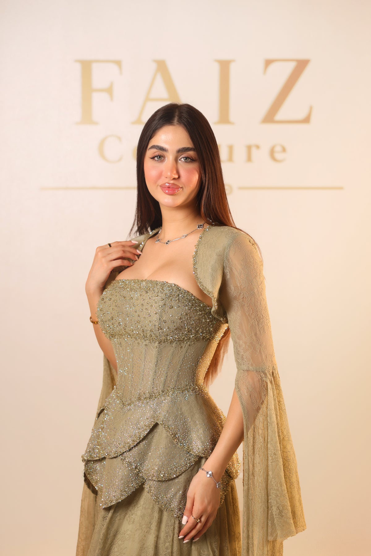 A woman modeling a strapless embellished gown in a champagne gold color with sheer draped sleeves, FAIZ COUTURE