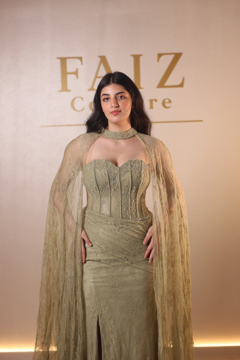 A woman modeling a floor-length sage green gown with a sheer draped overlay, FAIZ COUTURE