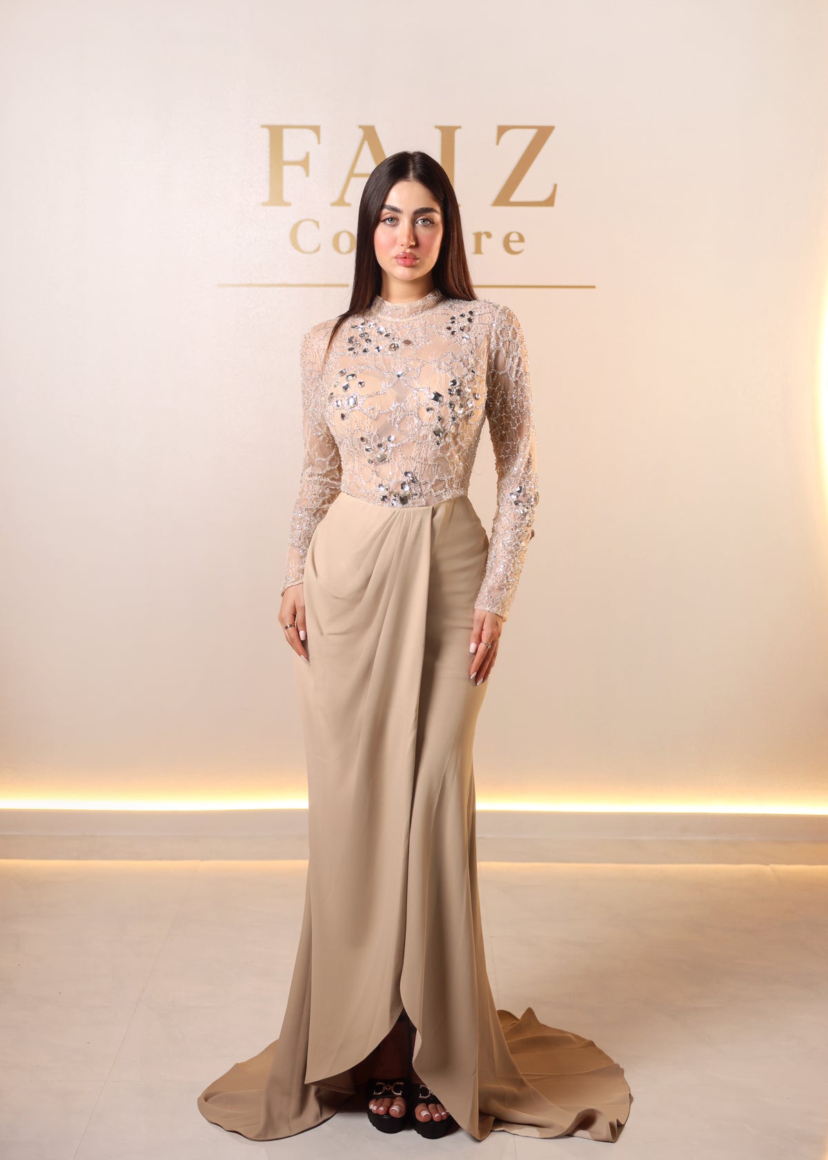 A woman models a floor-length beige evening gown with a heavily embellished lace bodice and a draped skirt, FAIZ COUTURE