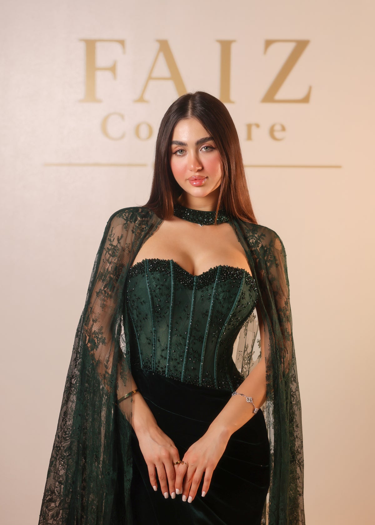 A woman wearing a dark green lace and velvet corset dress with a sheer lace cape and choker, FAIZ COUTURE
