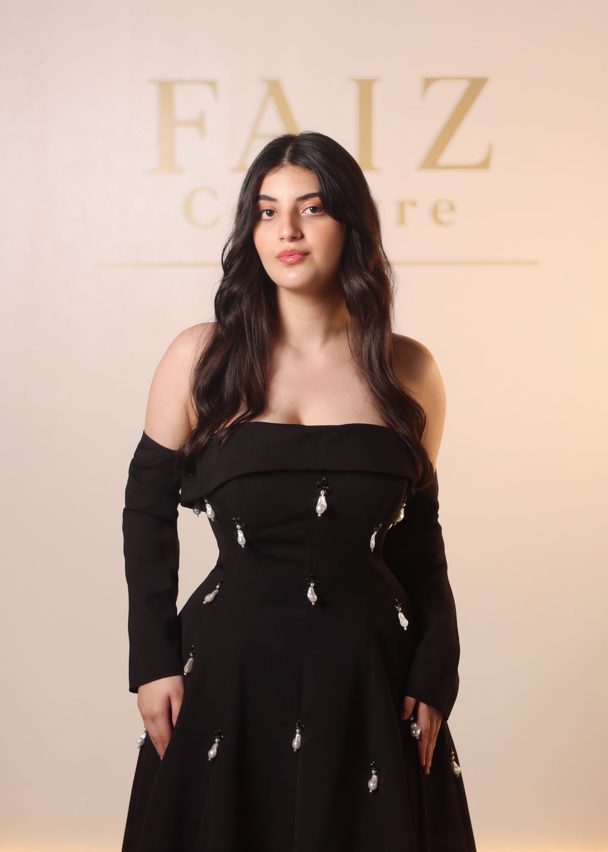 A woman wearing a black off-the-shoulder long-sleeve dress with small silver embellishments, Faiz Couture