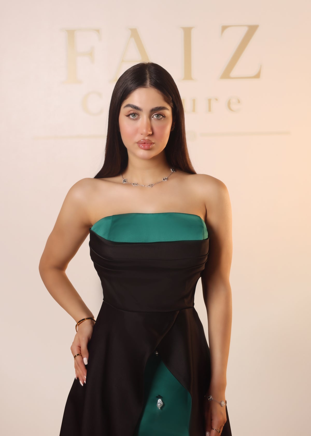 A woman modeling a strapless black dress with a teal green contrast band at the bust and matching green side panels, FAIZ COUTURE