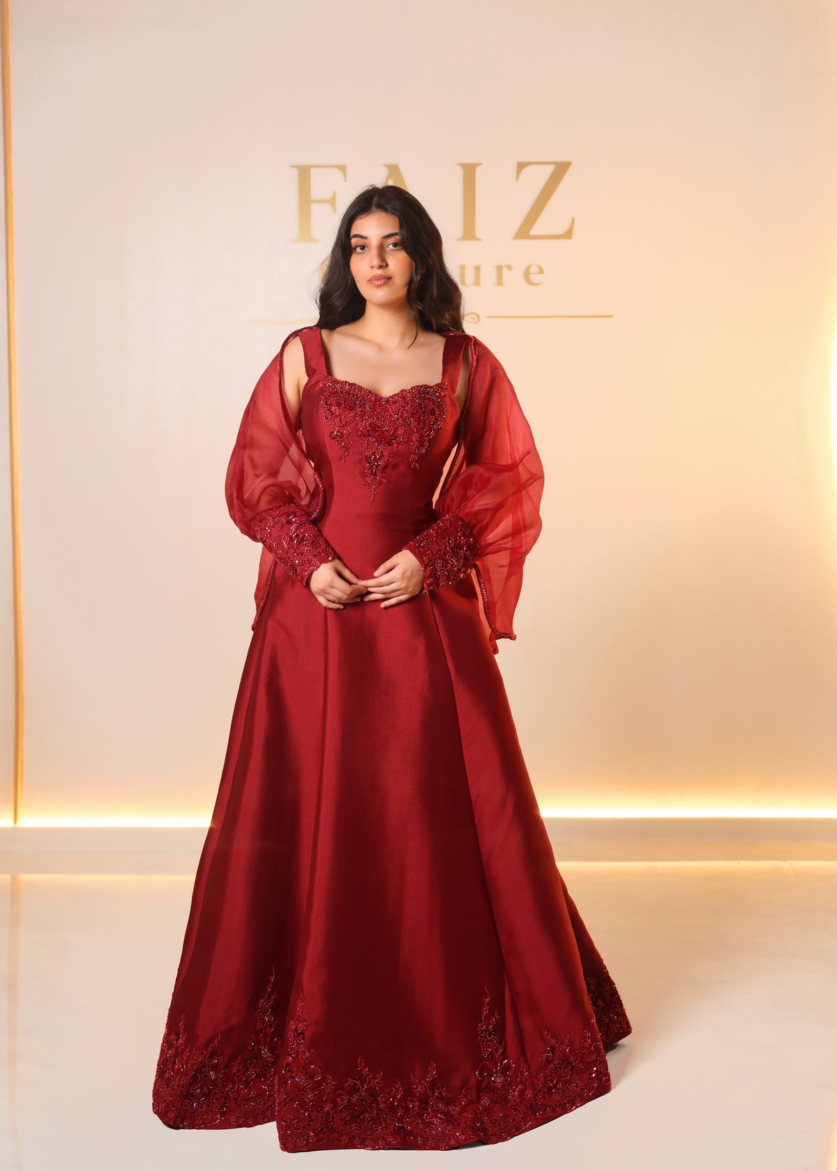 A woman models a floor-length burgundy red evening gown with sheer balloon sleeves and intricate floral embroidery, FAIZ COUTURE