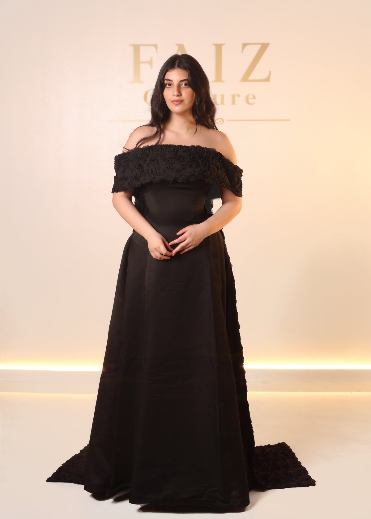 A woman modeling a floor-length off-the-shoulder black gown with textured ruffle detailing on the sleeves and side seams, FAIZ COUTURE