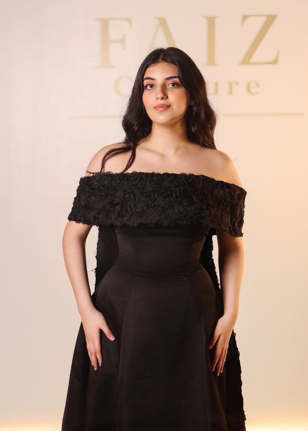 A woman wearing a black off-the-shoulder gown with a textured floral ruffle neckline, FAIZ COUTURE