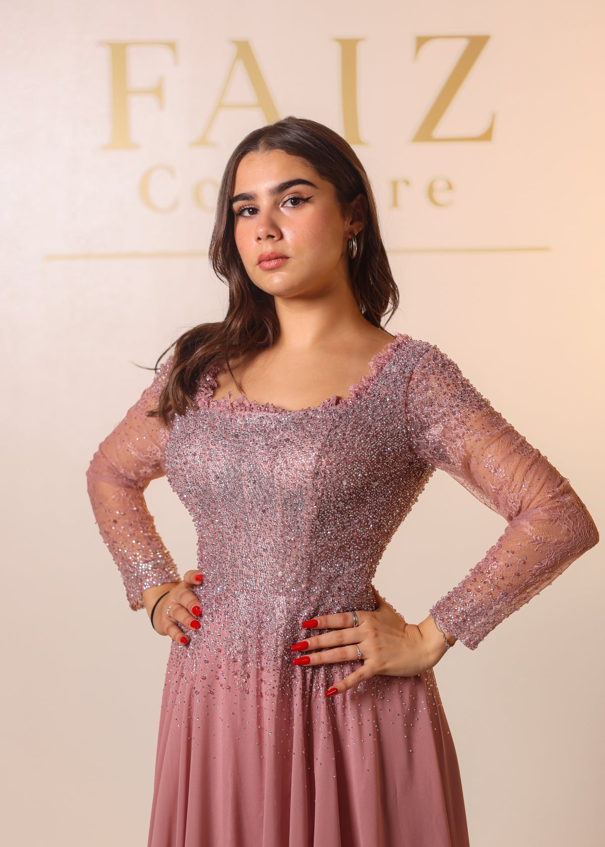 A woman modeling a dusty pink embellished gown with sheer long sleeves. FAOZ COUTURE