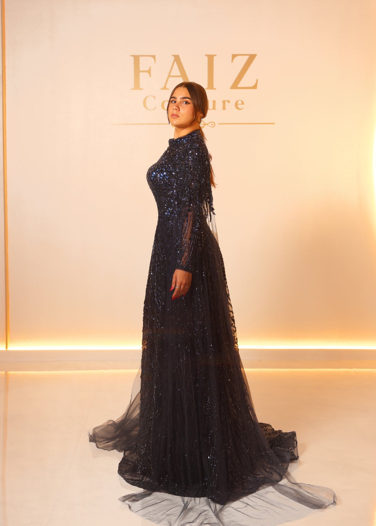 A woman modeling a floor-length black gown with dense sequin embellishments and sheer long sleeves, FAIZ COUTURE