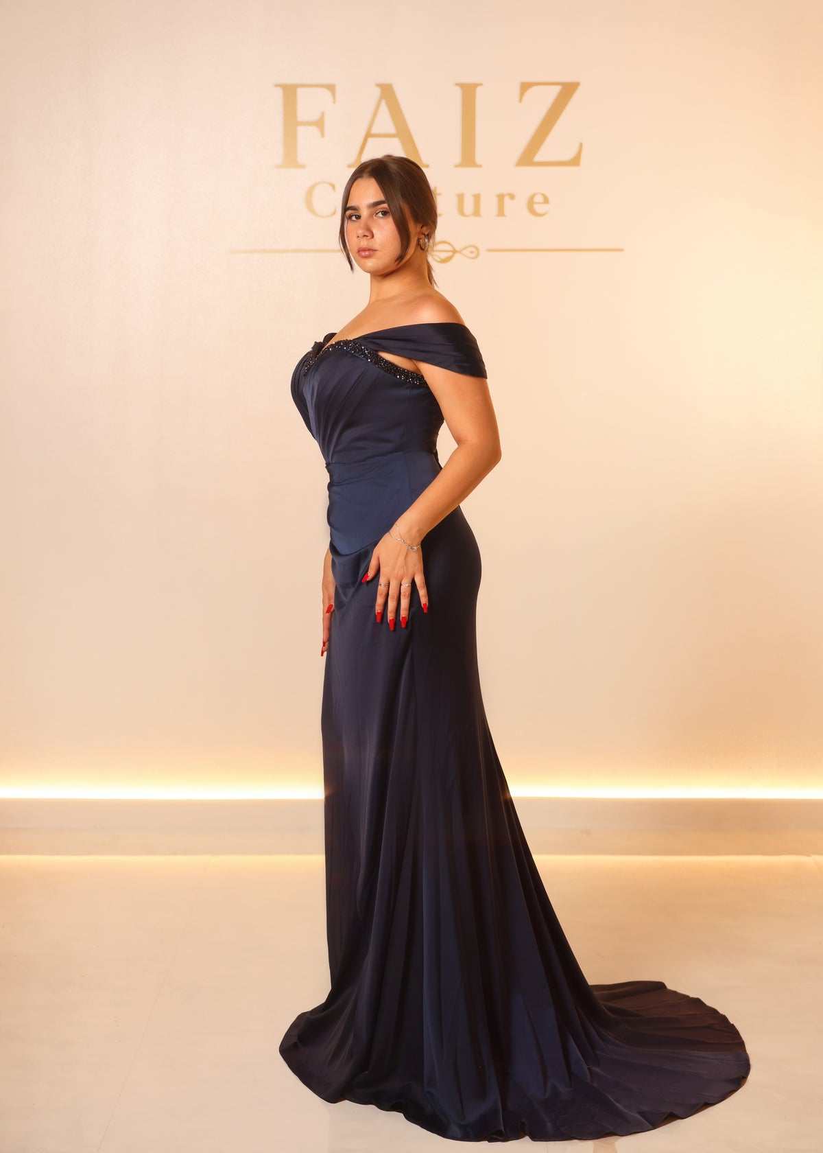 A woman modeling a floor-length navy blue off-the-shoulder gown with a fitted bodice and flowing train, FANIZ Couture