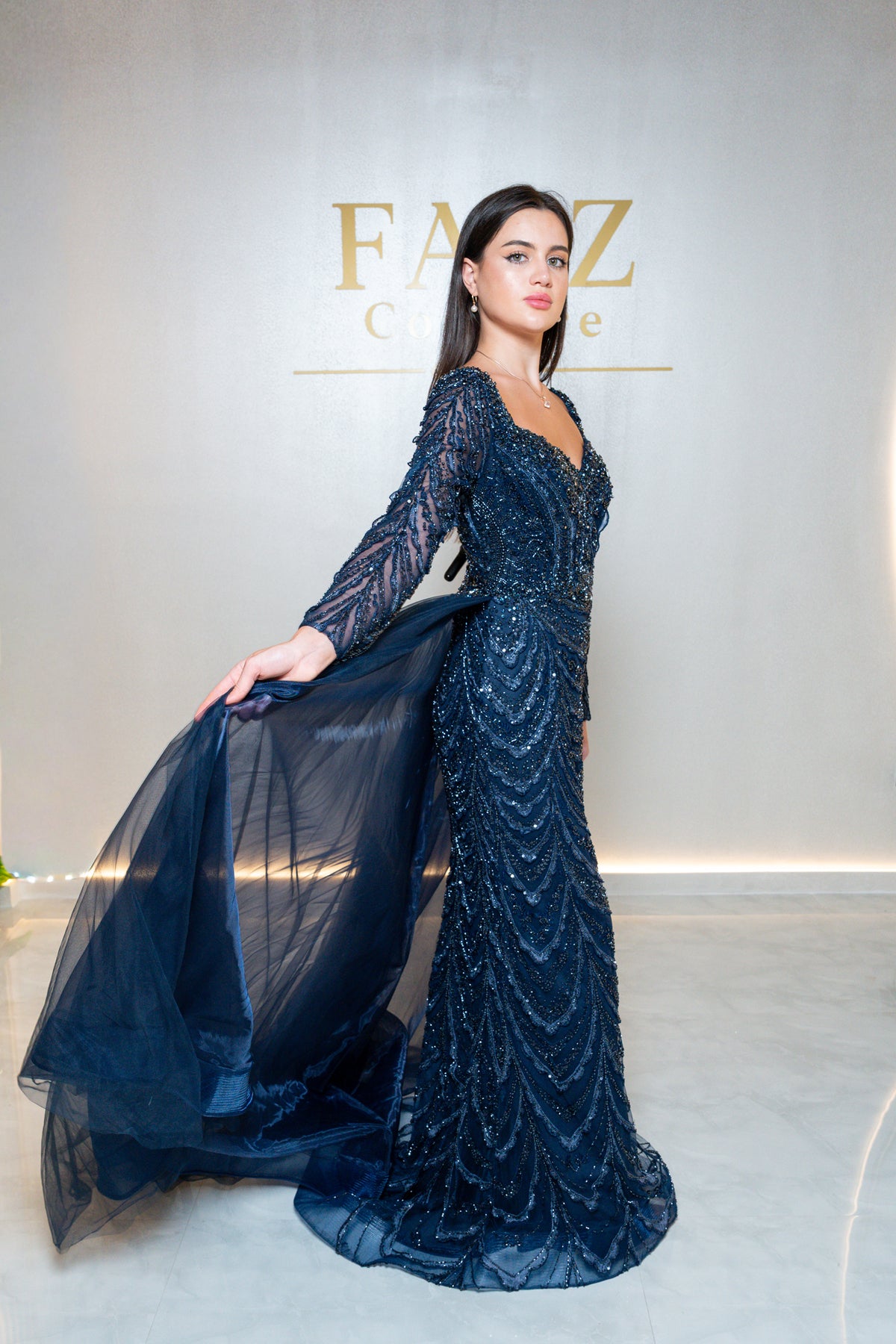 A woman modeling a long-sleeved, floor-length navy blue gown with intricate beaded and sequined detailing, FAIZ COUTURE