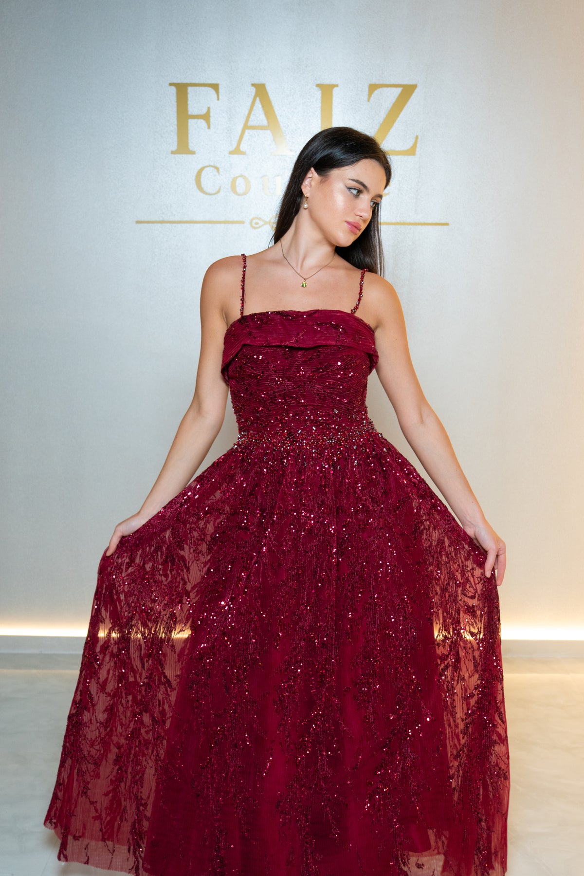 A woman modeling a deep burgundy lace and sequin ball gown with thin spaghetti straps, FAIZ COUTURE