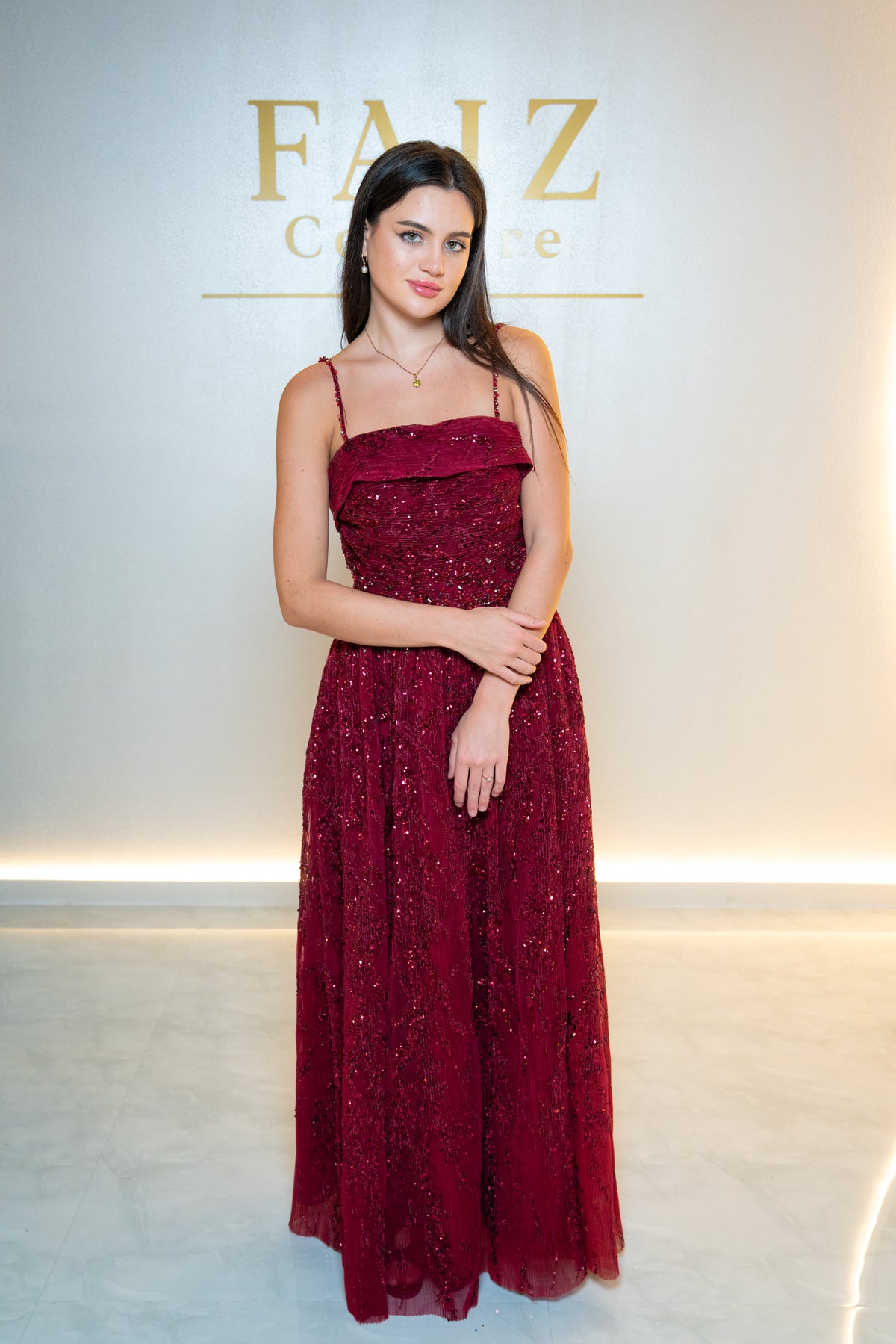 A woman wearing a floor-length burgundy sequined gown with thin straps, FAIZ COUTURE