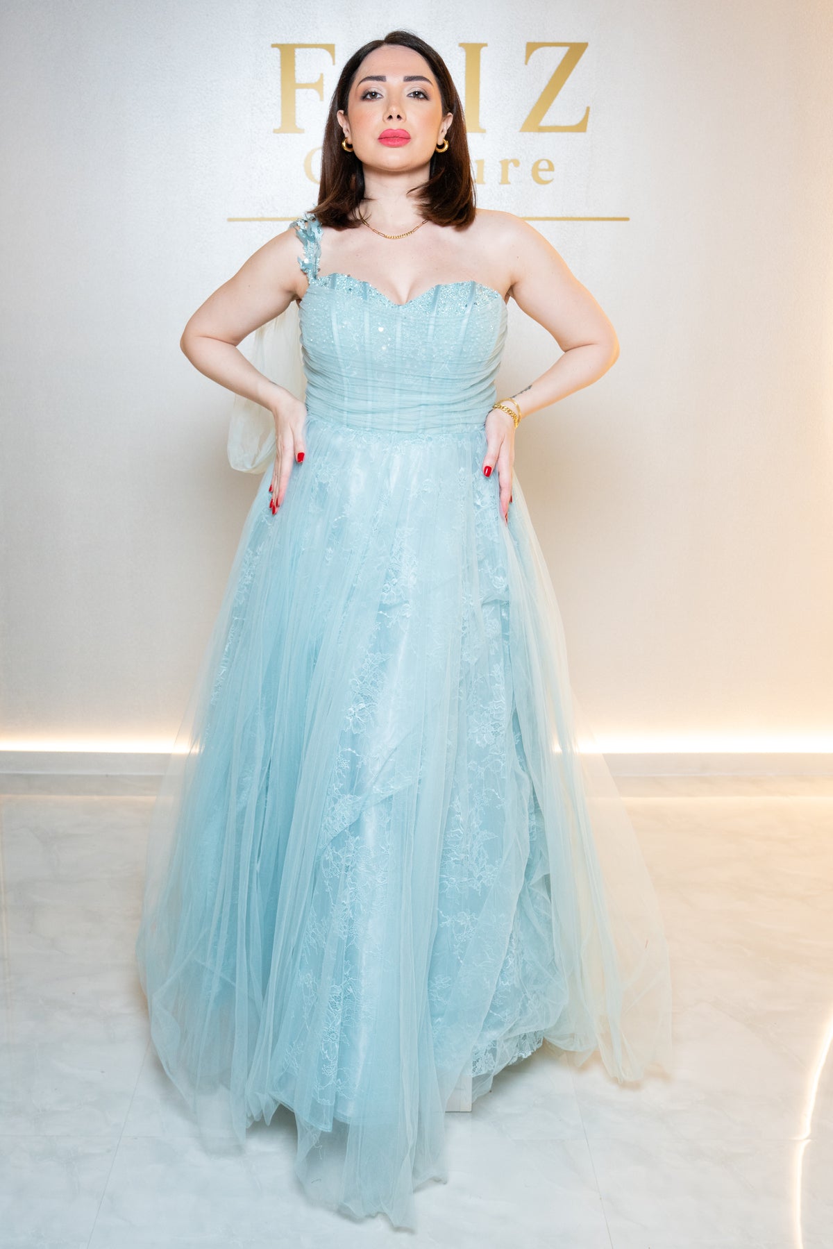 A woman modeling a light blue strapless tulle gown with lace applique and a sheer draped shoulder detail, FAIZ COUTURE