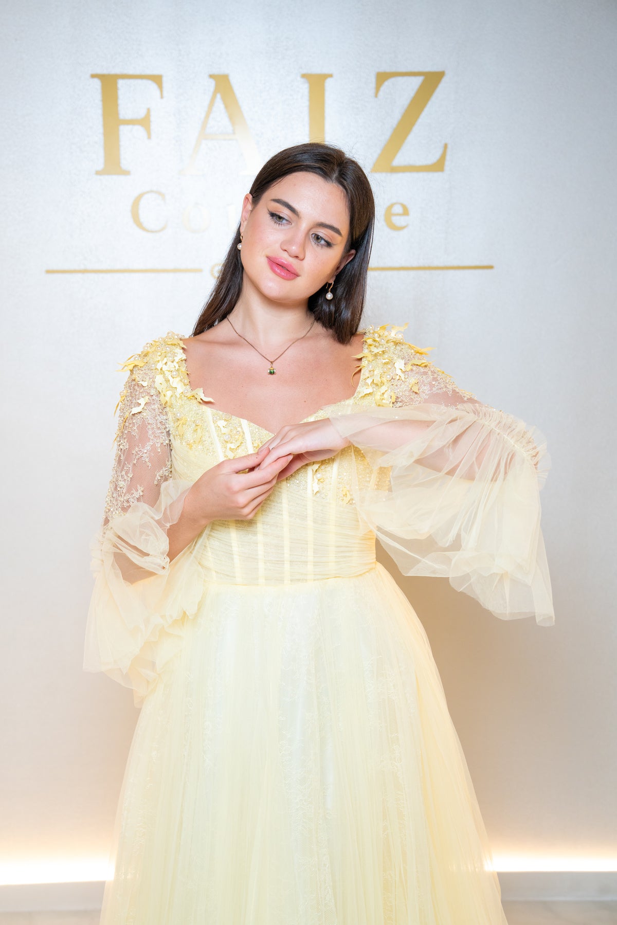 A woman wearing a pale yellow ballgown with sheer lace sleeves and a structured bodice, FAIZ COUTURE